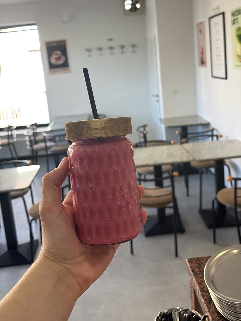 Fruchtiger Beeren-Smoothie im Glas, im Hintergrund der Gastraum des Eiscafés