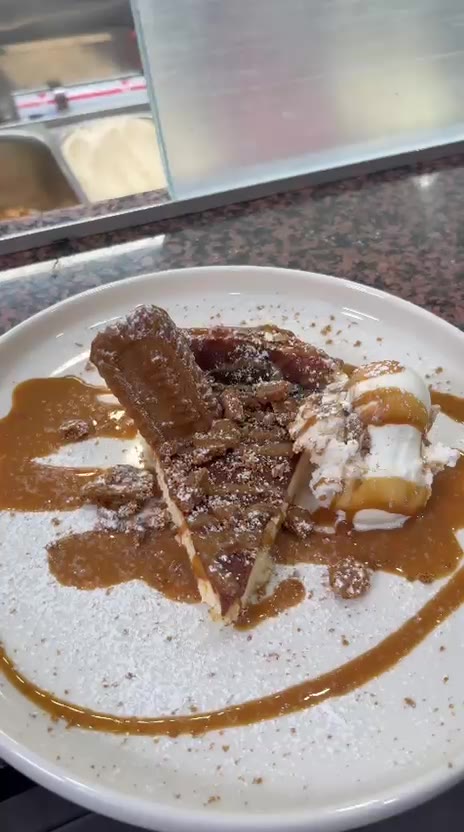 Lotus-Cheesecake mit Karamellsauce und Puderzucker auf weißem Teller