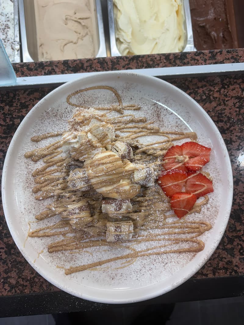 Waffel mit Karamell-Sauce, Puderzucker und frischen Erdbeeren vor der Eistheke im Eiscafé La Nocciola